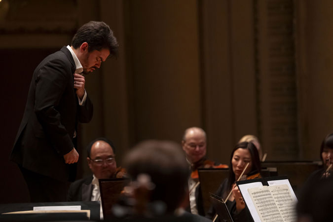 Shani prepares to conduct with his hand across his chest