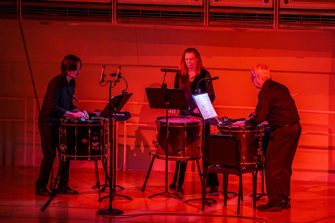 three percussionists awash in red light as they perform Quinn Mason's Weapon Wheel for three bass drums