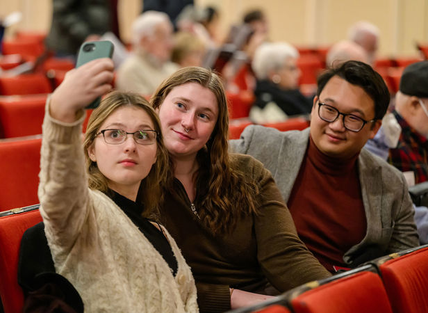 three young audience members smile for a selfie in their seats before the concert