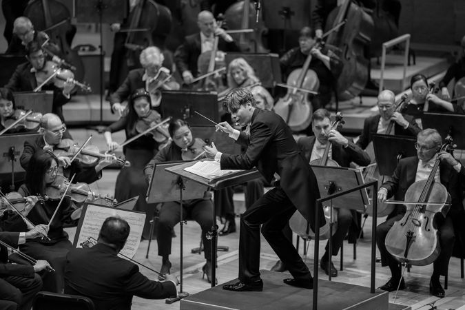 black and white: Klaus Mäkelä bends down on the podium, leaning in as he gestures to the CSO violin section