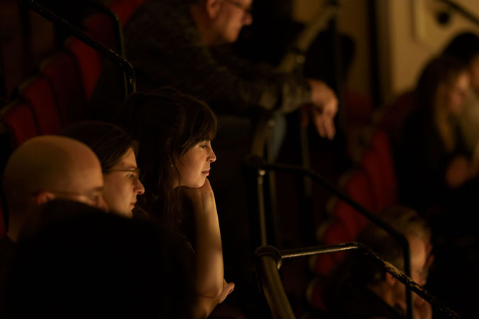 audience members watch intently from the upper balcony