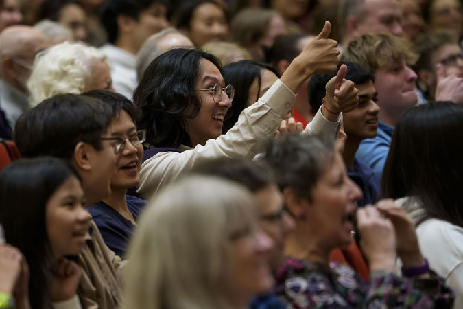 a young audience member in a tan button-up gives the artists a smile and a thumbs up