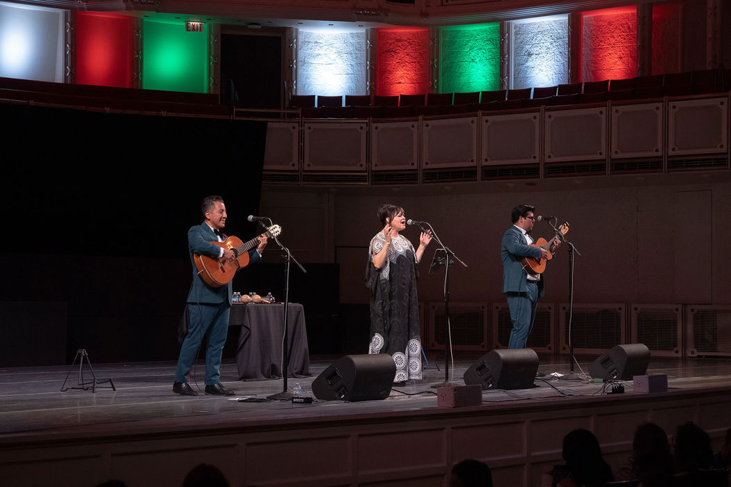 Bolero trio Tres Souls performs on stage while the lights behind the Orchestra Hall stage reflect the colors of the Mexican flag