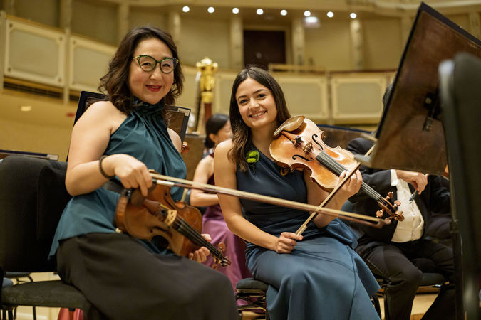 CSO assistant concertmaster Yuan-Qing Yu and violin Gabriela Lara smile at the camera before warming up on stage