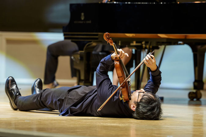 Brett Yang plays a note while lying down on stage
