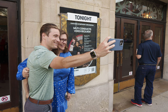 A couple takes a selfie on Michigan Avenue in front of the concert poster