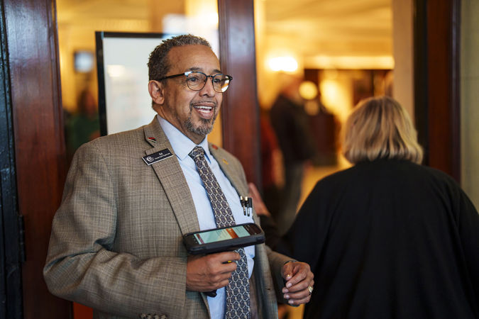 house staff supervisor Ed scans an audience member's ticket, looking dapper in a gray suit coat and blue tie