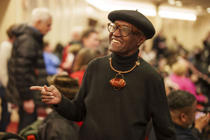 an audience member wearing a hat and colorful necklace takes their seat